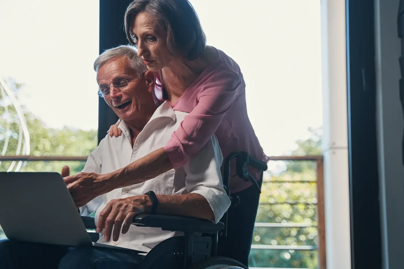 An older man uses a laptop, with an adult woman standing beside him.